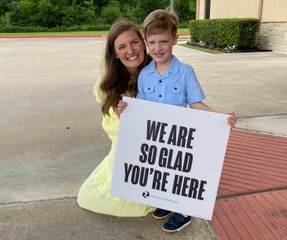 woman and boy holding sign saying We are so glad you're here